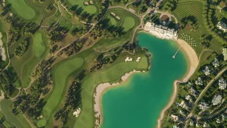 aerial overhead view of a turquoise lake next to a golf resort with beautiful abstract patterns, sand traps, trees tennis courts, and a