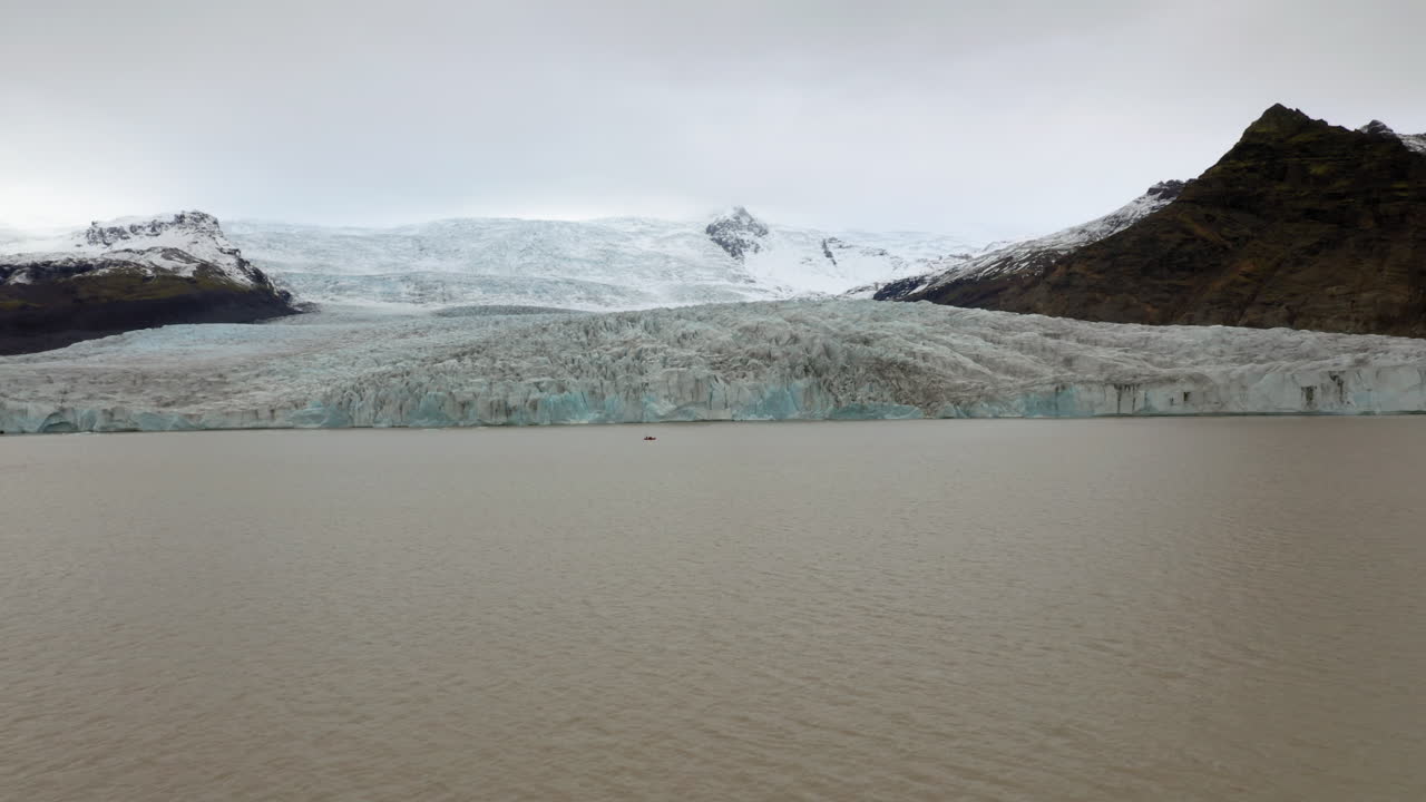 antena: volando hacia un pequeño bote con turistas cerca del glaciar fjallsarlon en el sur de islandia durante un día nublado