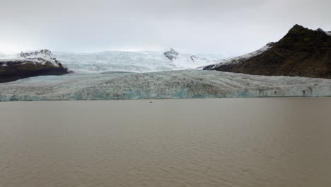 Aerial:-Flying-towards-a-small-boat-with-tourists-near-Fjallsarlon-glacier-in-south-iceland-during-an-overcast-day