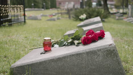 side view of red roses and a candle on tombstone in a gravevard