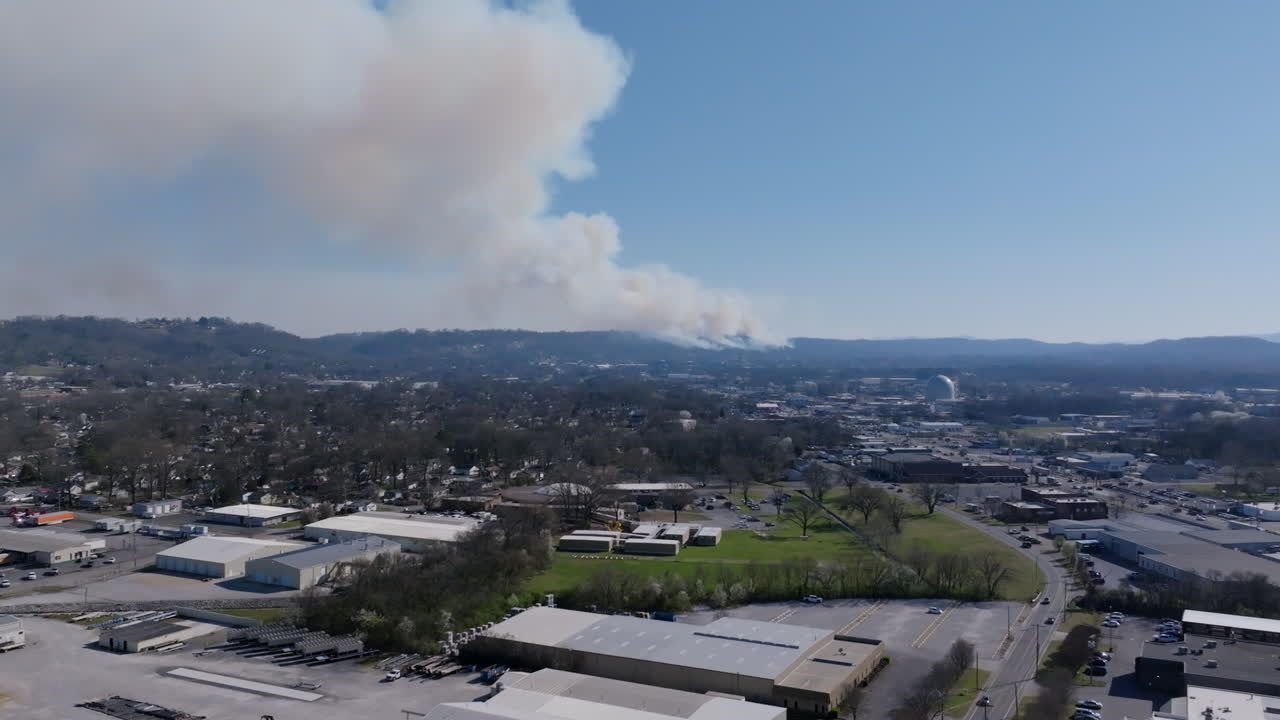 Aerial drone footage that is panning across an industrial area of a city with a large wildfire going on in the background.