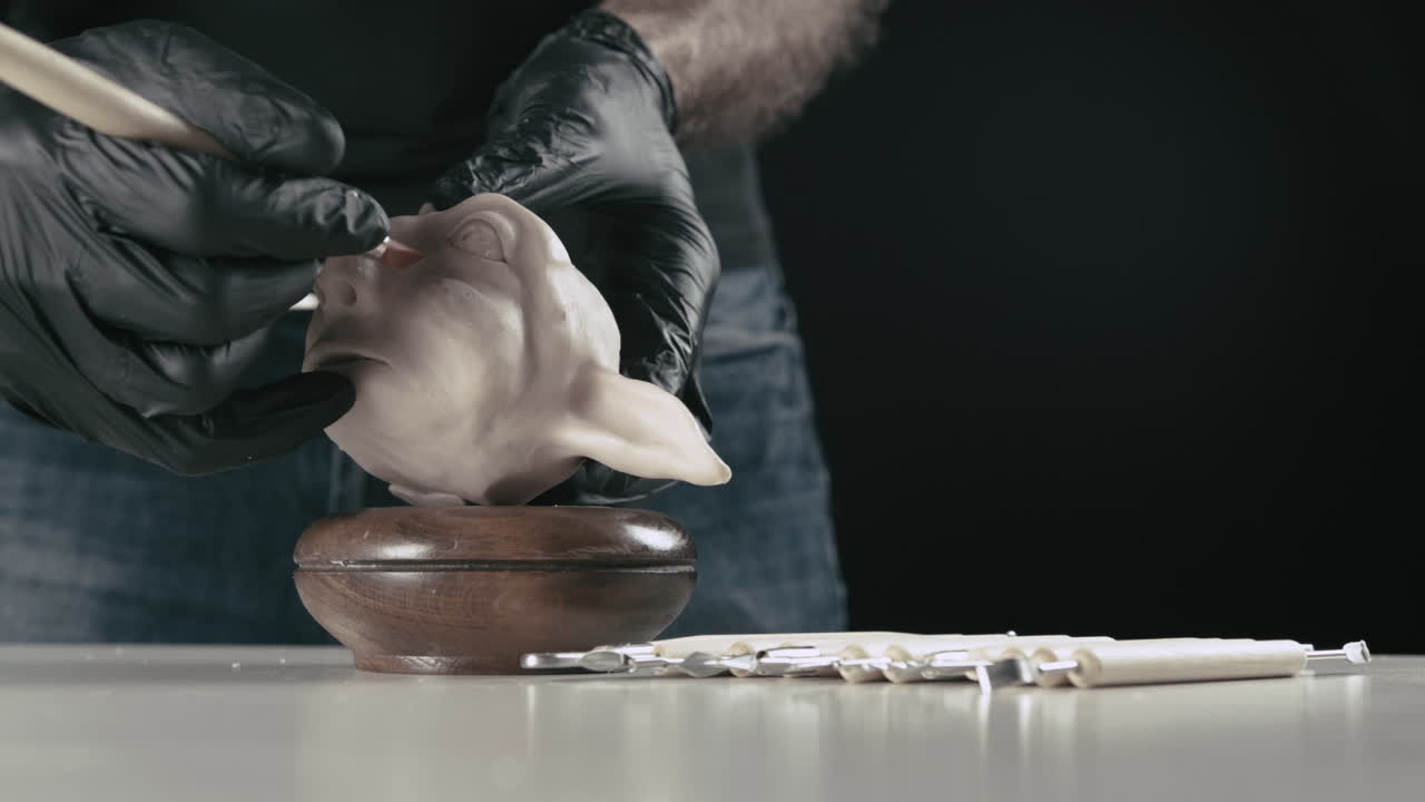 artista termina una cabeza de títere de plastilina con una herramienta de modelado.