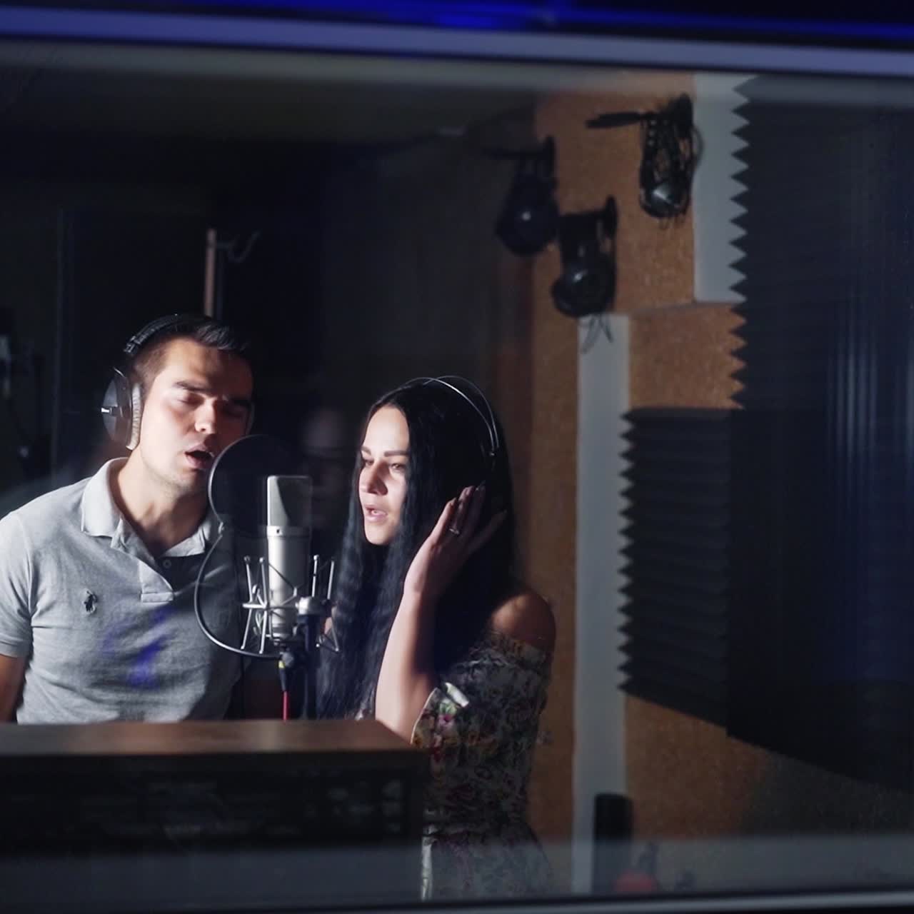 Beautiful couple of singers singing in the studio. Man and woman recording song and music in the dark room of studio