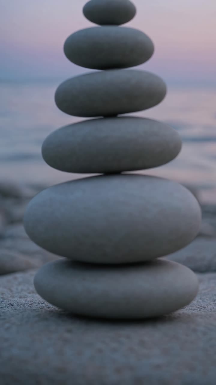 Close-up video of stacked smooth stones on a beach at sunset, shot from a low angle