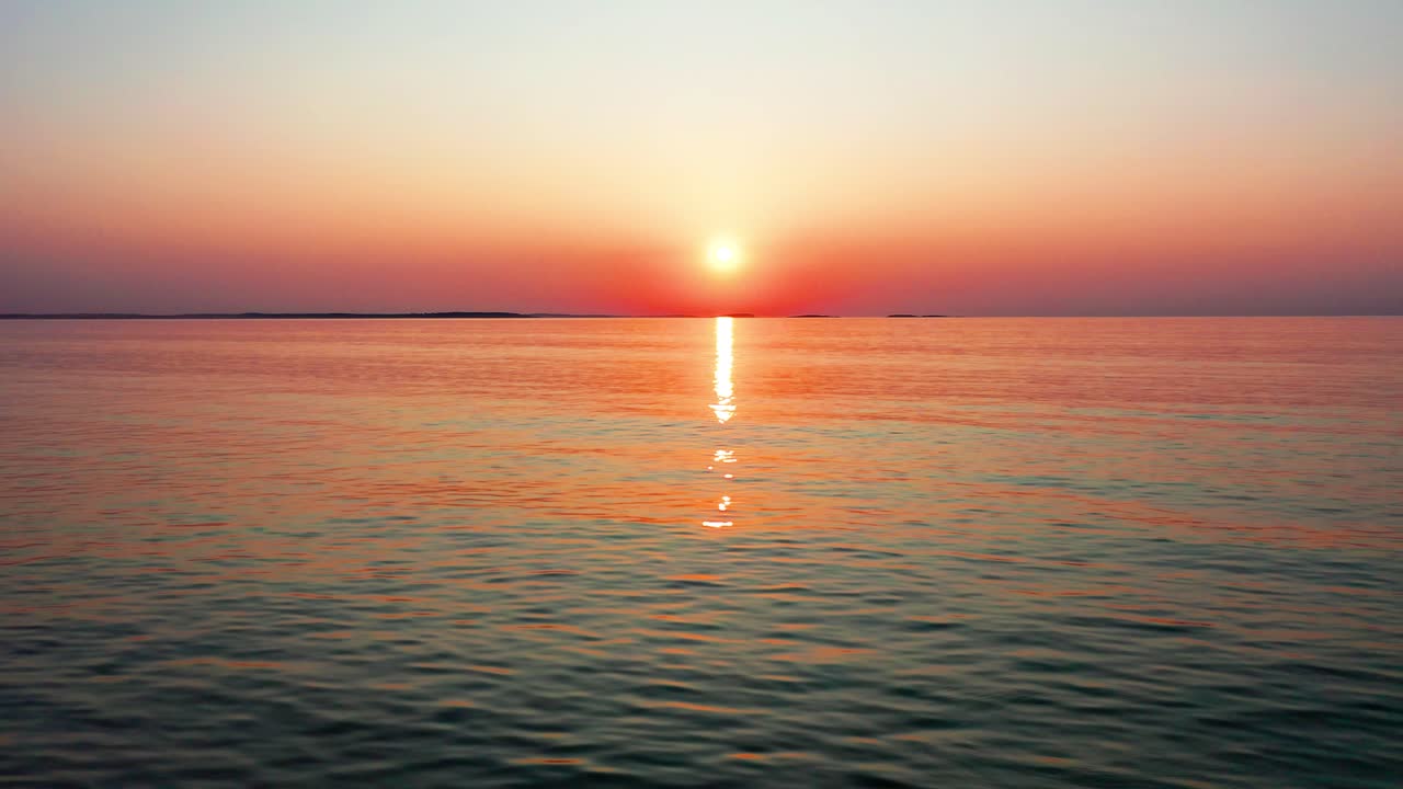 바다의 아름다운 일몰, 밝고 반이는 태양, 화려한 하늘과 물과 함께 평화로운 물결의 물결 위에 다채로운 빨간색, 오렌지색, 보라색 및 노란색 반사.