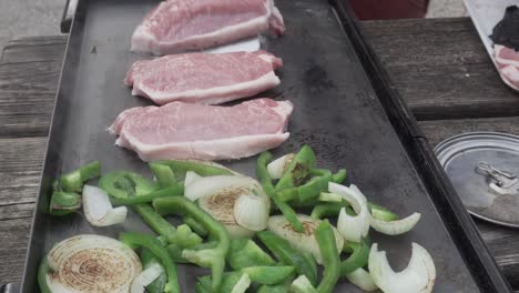 pork chops and sliced green peppers and onions cooking on griddle hot plate outside at campground in 4k 29.97p 30p