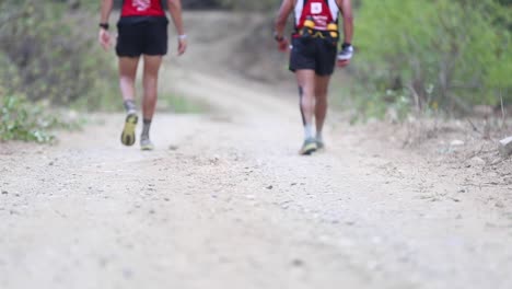 Group-of-tired-marathon-athletes-walking-on-a-dirt-road-along-through-bush-forest-jungle-in-rural-beautiful-nature-of-Ecuador-50-fps