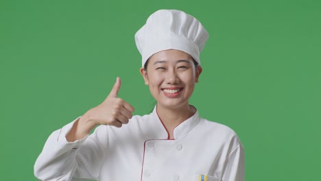 Close Up Of Asian Woman Chef Smiling And Showing Thumbs Up Gesture To Camera While Standing In The Green Screen Background Studio