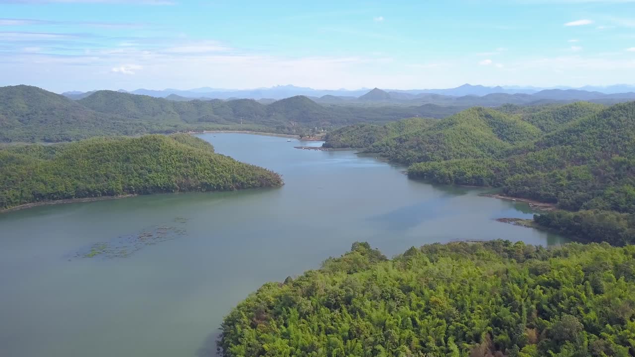 vuelo aéreo panorámico sobre un lago soleado rural remoto con bosques y montañas en el horizonte