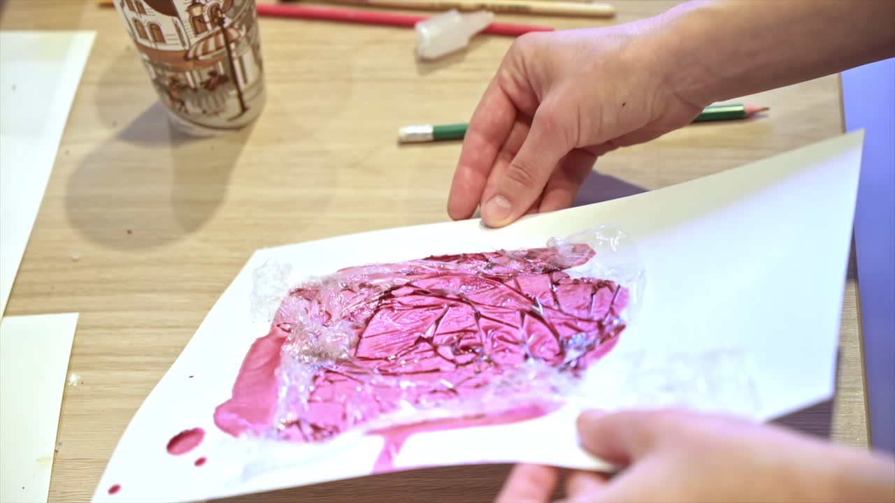 A woman in a studio painting on paper with red wine and cellophane, close view, slow motion