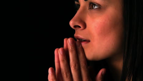 Upset-brunette-praying-on-black-background