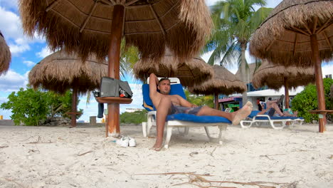 An-Indian-man-relaxes-under-an-umbrella-hut-on-Chen-Rio-beach-on-the-island-of-Cozumel,-Mexico