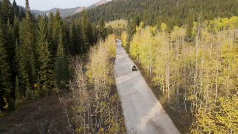 all terrain vehicle atv driving on country road through mountain forest, aerial