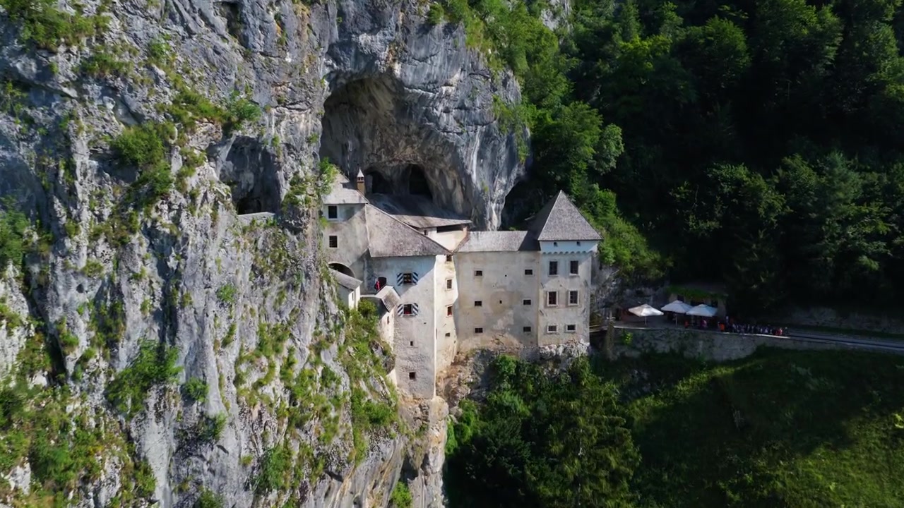 A Cave Beneath The Towering Rock Wall Below Predjama Castle In Inner Carniola, Slovenia. Aerial Forward Shot