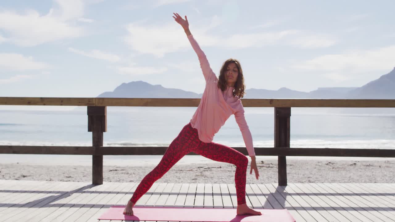 mujer de raza mixta practicando yoga saludable al aire libre, de pie y estirándose junto al mar