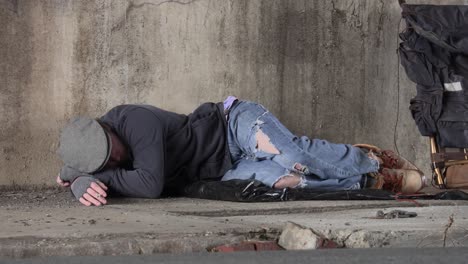 drunken homeless man passed out asleep on the sidewalk under a overpass with a lit cigarette still in his hand