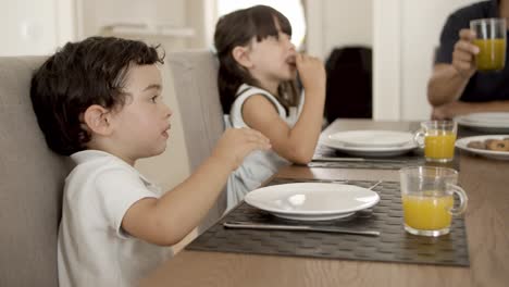 Little-kids-eating-cookies-at-dining-table-with-dish