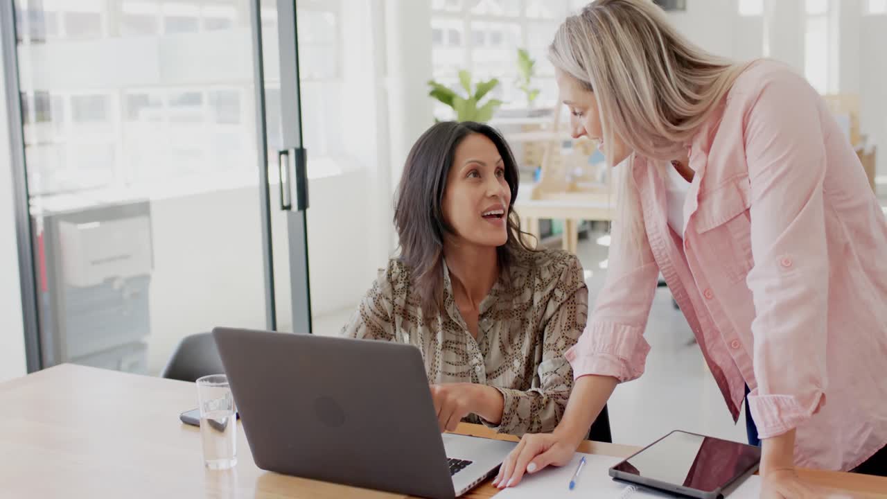 mujeres de negocios felices y diversas discutiendo el trabajo con una computadora portátil en la oficina en cámara lenta