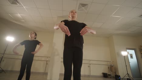 a group of young ballet students in black dancewear practicing positions in a spacious ballet studio with wooden flooring and wall-mounted barres. focused expressions and synchronized movements.