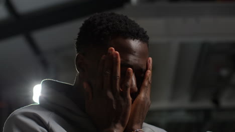 close up low key lighting shot of unhappy and depressed young man with head in hands shaking head