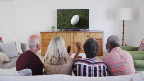 senior diverse friends watching tv with rugby ball at stadium on screen