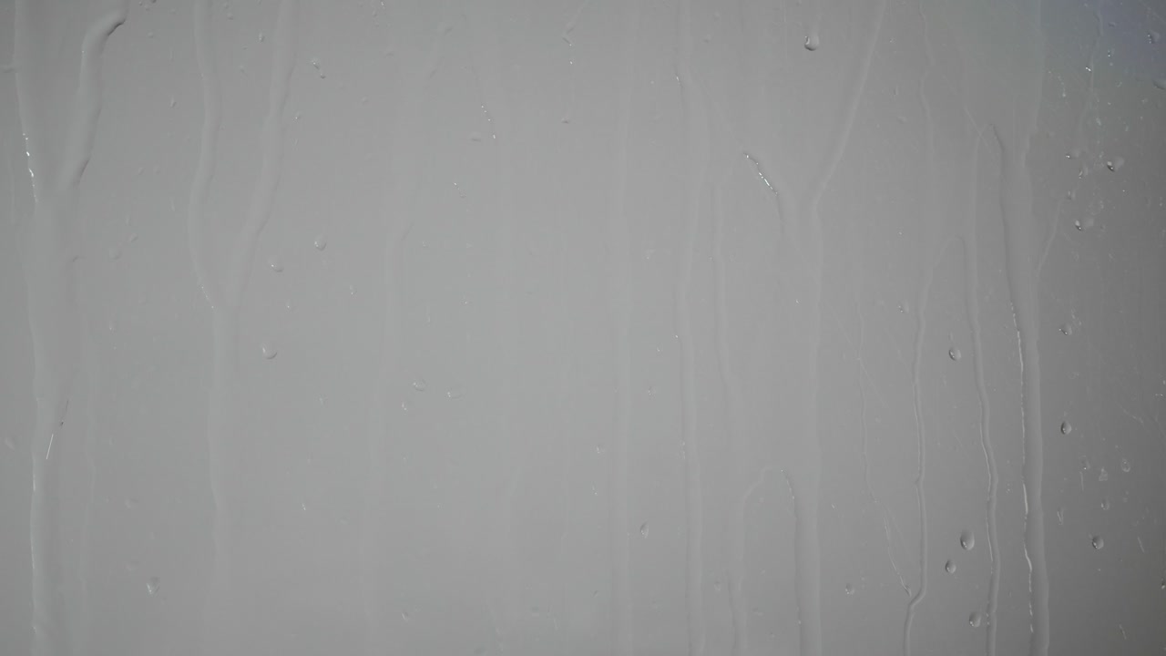 Gocce d'acqua che scivolano su una superficie di vetro trasparente