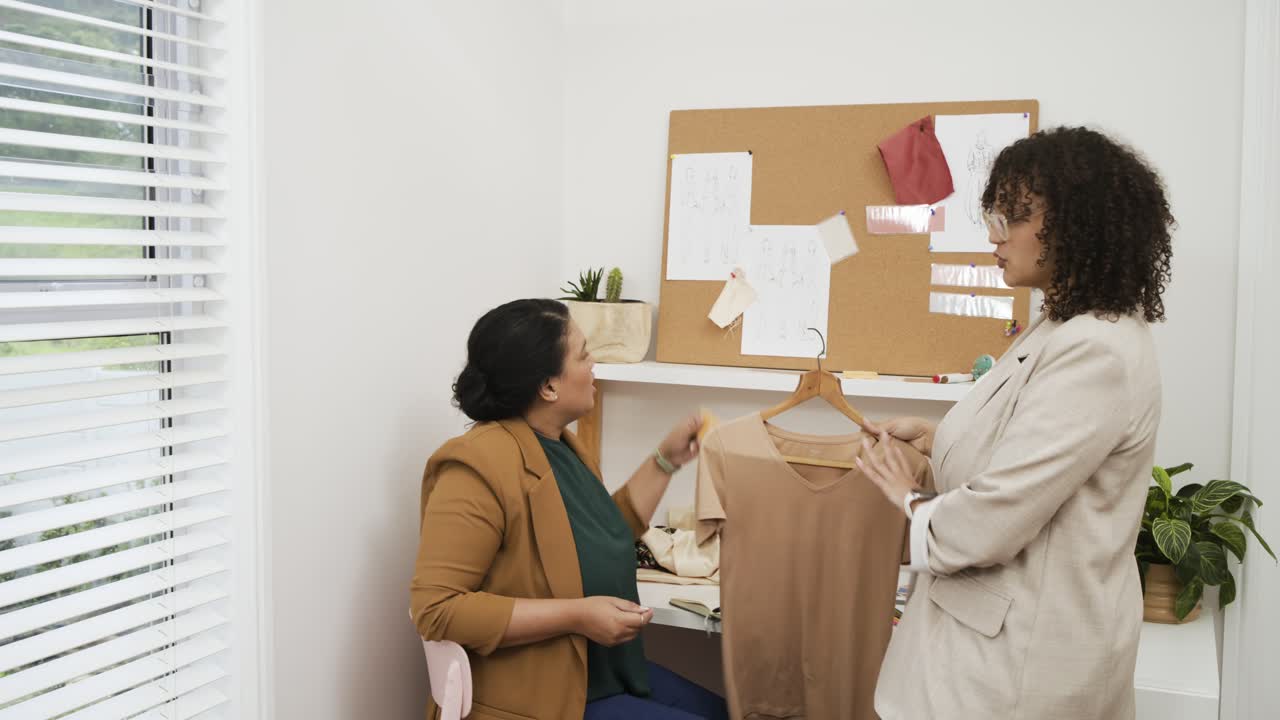 Un collega che indica design appuntati guida una donna nella scelta di una camicetta beige per l'abbinamento colori alla scrivania