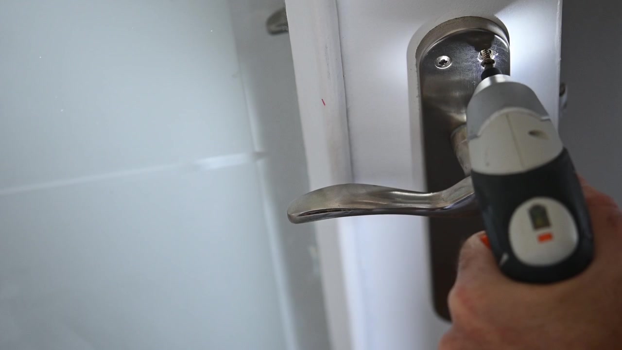 Close-up of a battery-powered cordless screwdriver screwing in a doorknob screw