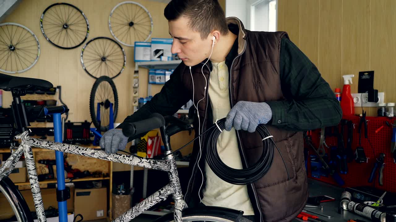 joven mecánico propietario de un taller de reparación de bicicletas está arreglando una bicicleta sosteniendo un fajo de alambre y fijándola en el marco de la bicicleta. concepto de pequeña empresa y mantenimiento.
