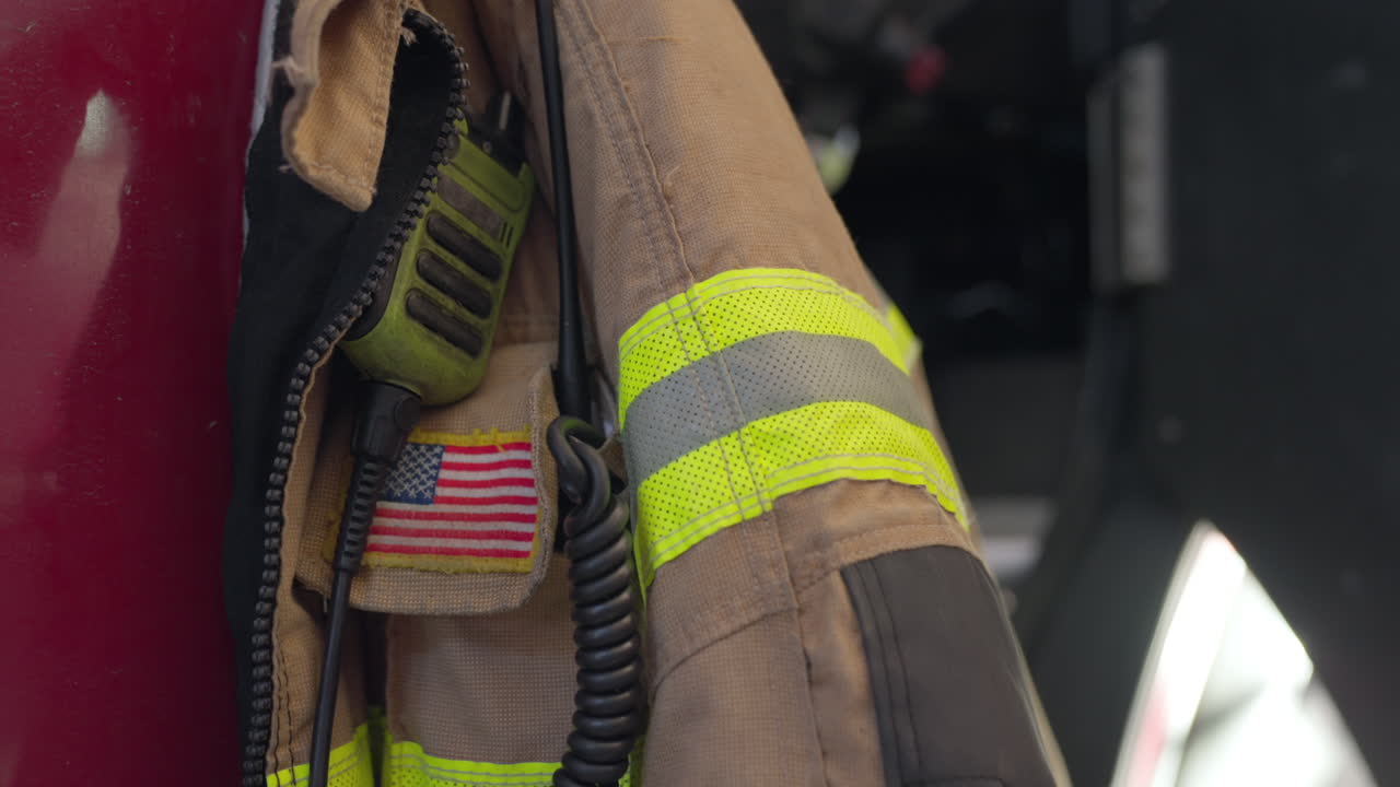 Fireman jacket known as bunker or turnout safety gear hanging on firetruck door ready to be used in case of emergency. Special equipment for firefighters in station. USA flag embedded on jacket