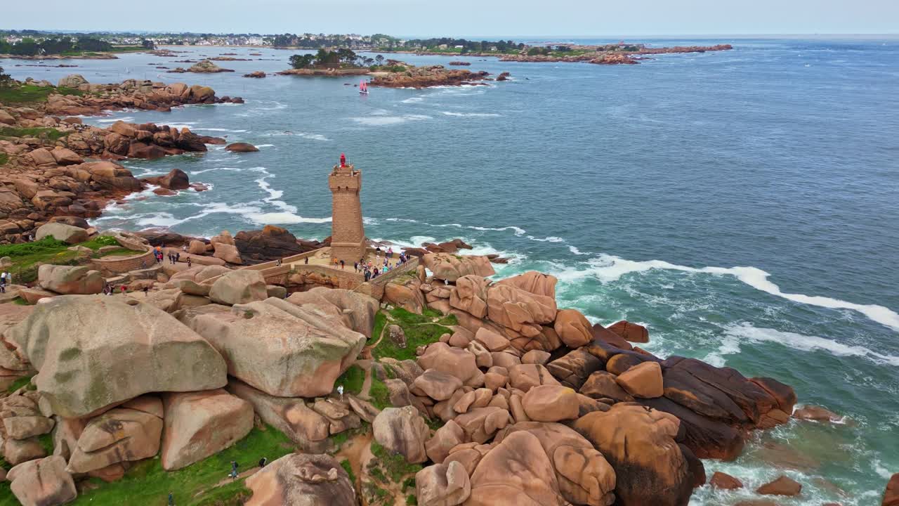 Mean Ruz lighthouse on Pink Granite Coast, tourists exploring coast of Ploumanac'h, Brittany, France. Aerial drone forward at low altitude