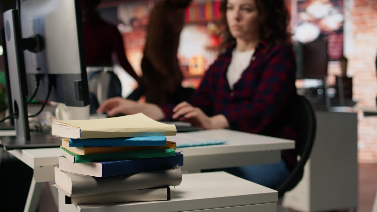 pila de libros en el escritorio de la oficina de inicio frente a la mujer trabajando, primer plano
