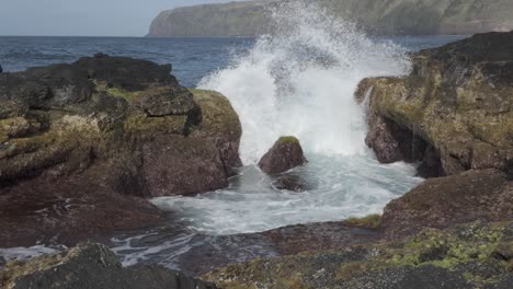 Las-Olas-Rompen-Contra-Los-Acantilados-Rocosos-En-Mosteiros,-Sao-Miguel-Con-Una-Colina-Distante,-Vibrante-Y-Dinámica.