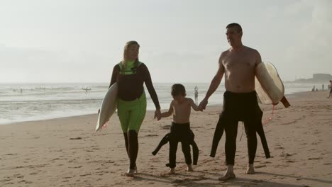 family with surfboards walking on sandy beach