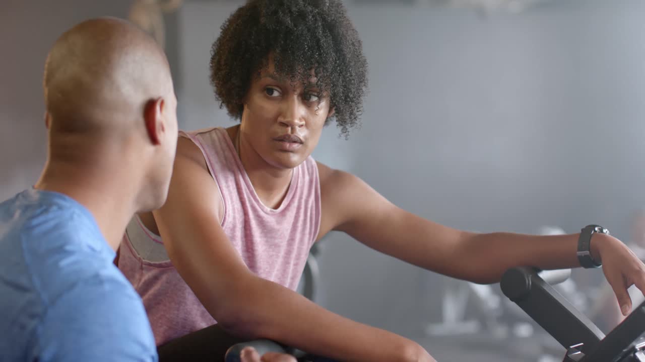 entrenador masculino diverso y mujer enfocada en bicicleta elíptica hablando en el gimnasio en cámara lenta