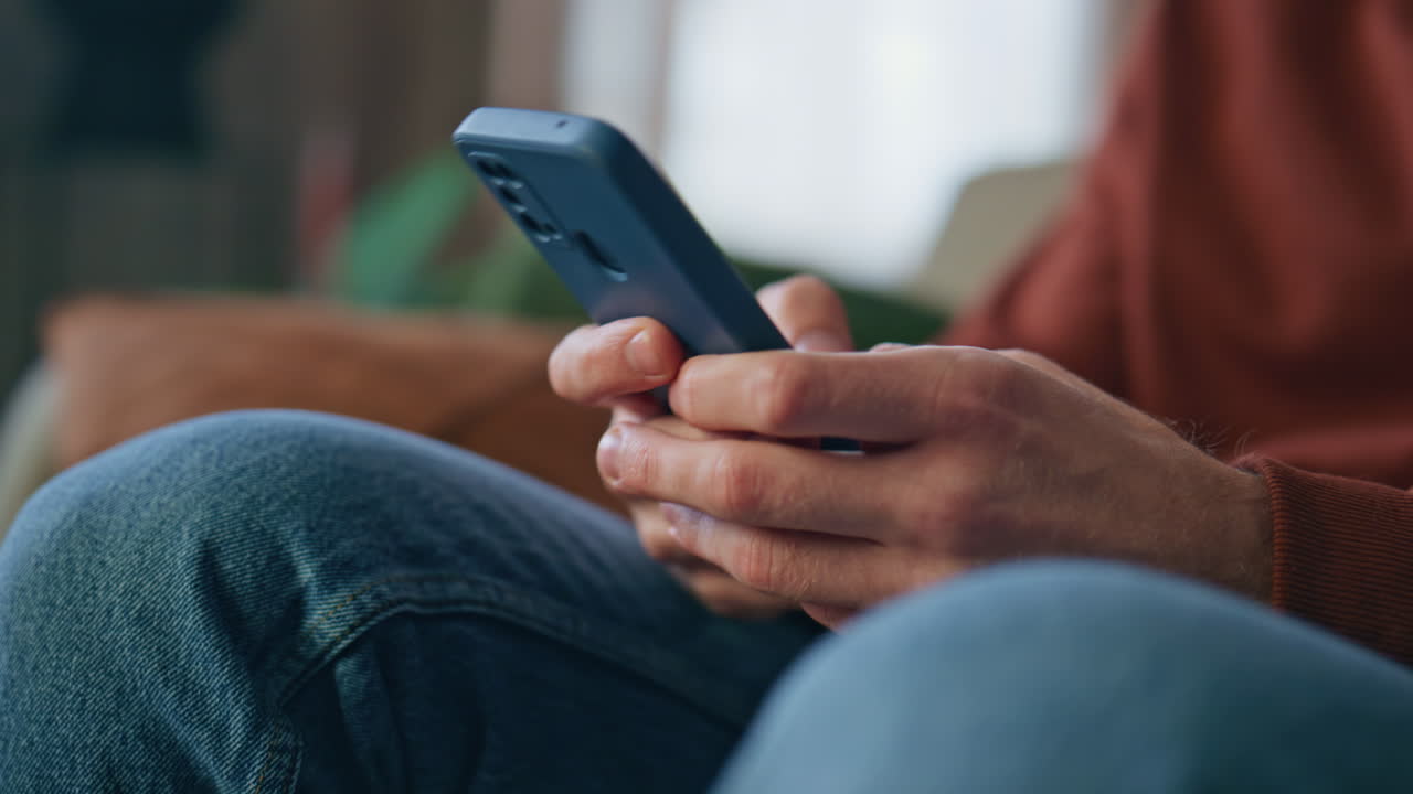 Closeup man hands messaging smartphone at home close up. Cheerful guy laughing
