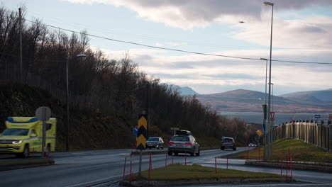 traveling vehicles over asphalt road with fjord and mountain background during sunset in tromso, norway