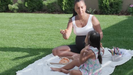 una madre e hija disfrutan de un picnic de verano al aire libre en un césped cubierto de hierba, compartiendo pizza y pasando tiempo de calidad juntos en un día soleado. la escena de unión familiar refleja ocio y relajación.