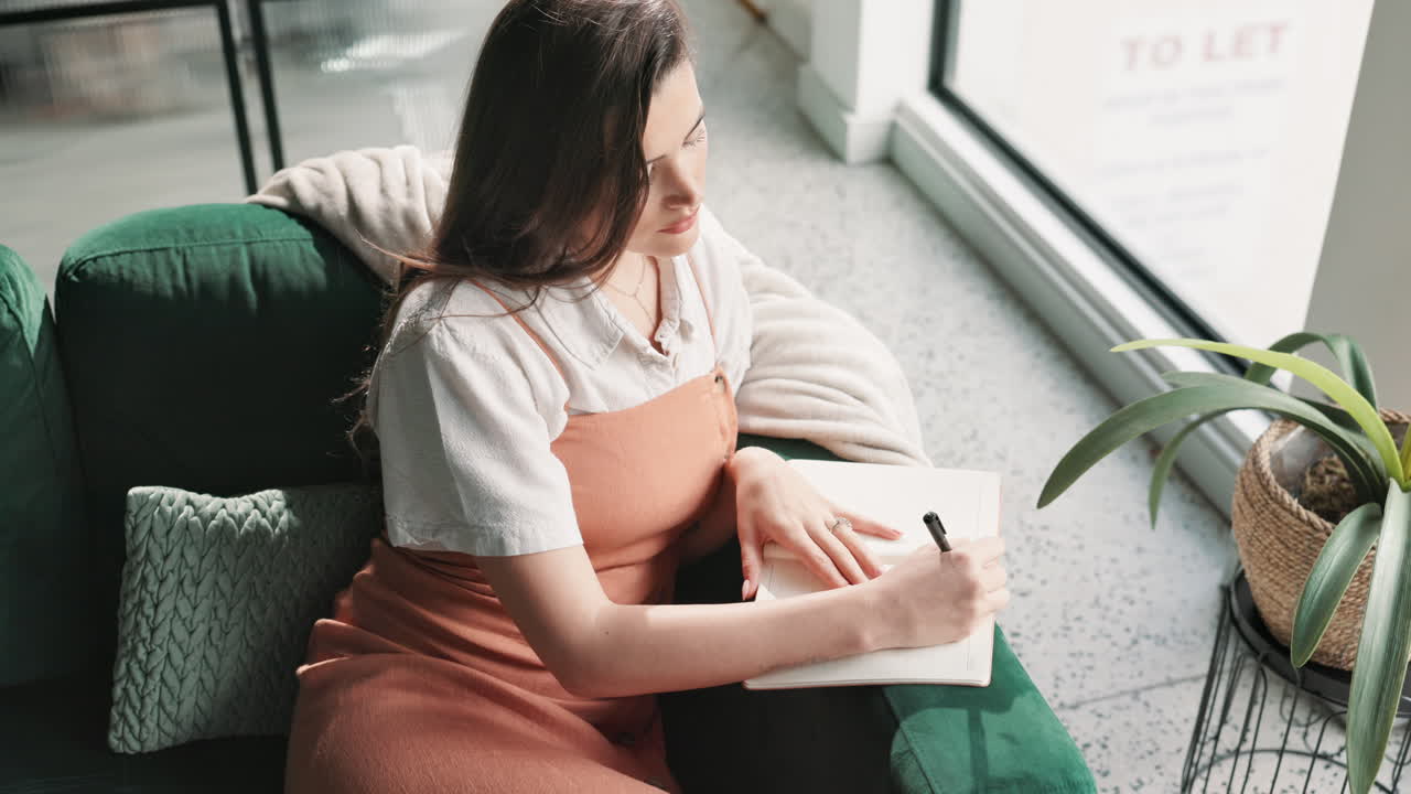 Woman writing in a journal on a sofa
