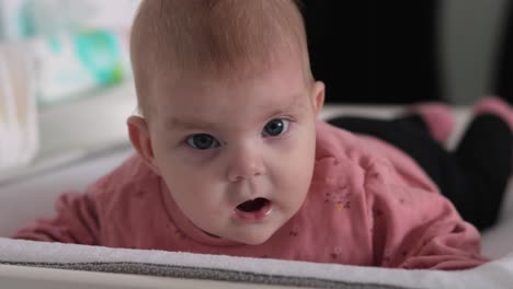 Baby-girl-lying-in-prone-position-on-mat,-moves-arms-and-legs,-facing-camera