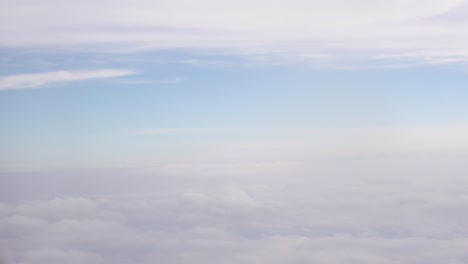 pov of a passenger looking out an airplane window at the sunny blue sky and fluffy clouds