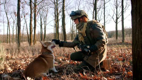 young pretty redhead woman in military uniform armed with rifle playing with dog