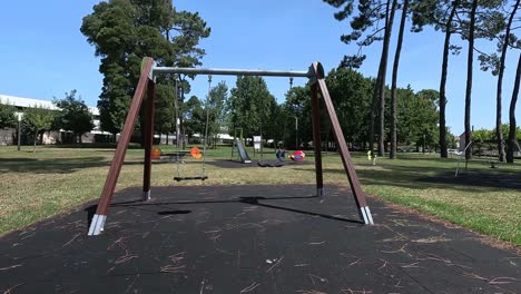 Swings-on-rubber-platform-keep-swinging-in-motion-without-people-in-the-landscaped-public-park-with-slide-and-more-games-back,-residential-area,-sunny-day,-close-up-shot