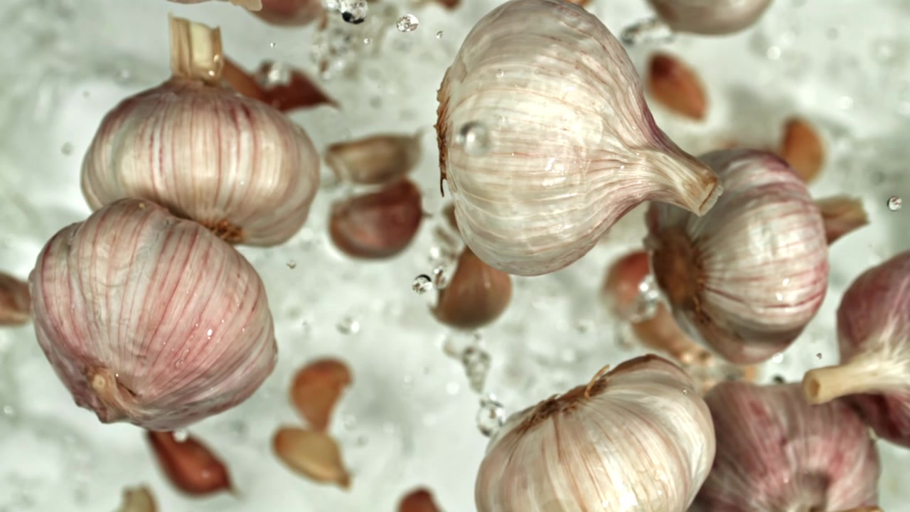 Bulbi e spicchi d'aglio che schizzano in acqua su sfondo bianco