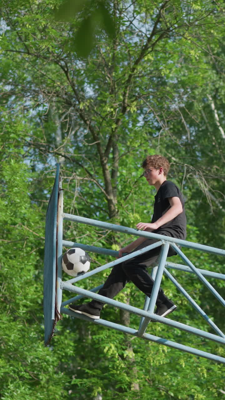 un niño se sienta en un equipo al aire libre de hierro azul, moviendo su mano izquierda y pierna hacia atrás mientras una pelota permanece atascada en el marco