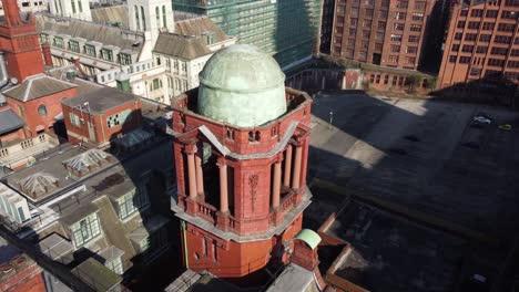 aerial drone flight over oxford road showing the refuge buildings smaller green dome alongside the rooftops and architecture below in manchester city centre