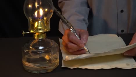 person writing with a quill pen and oil lamp