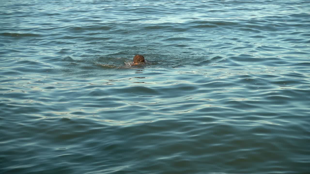 The man swims in the sea in the summer evening. Slow motion