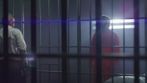 el empleado de la prisión le da el teléfono al criminal a través de barras de metal.