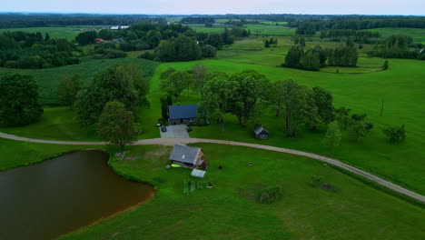 Aerial-of-charming-house-by-rural-pond,-embraced-by-lush-greenery